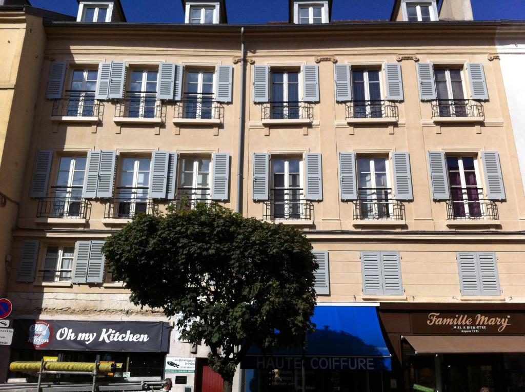 un grand bâtiment avec des fenêtres blanches à volets et un arbre dans l'établissement bel appartement chic et cosy 78100, à Saint-Germain-en-Laye
