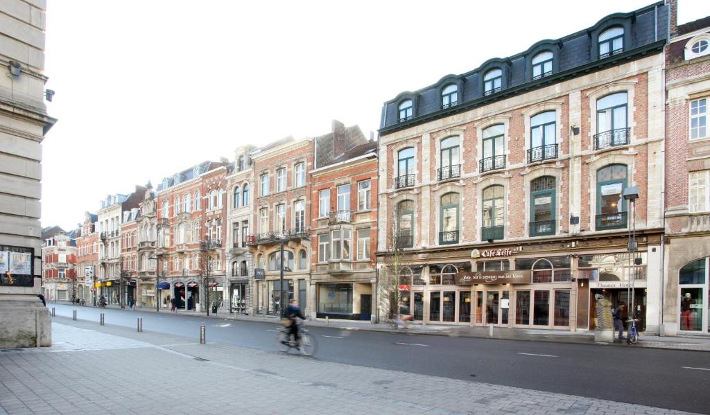 a man riding a bike down a street with buildings at Theater Hotel Leuven Centrum in Leuven