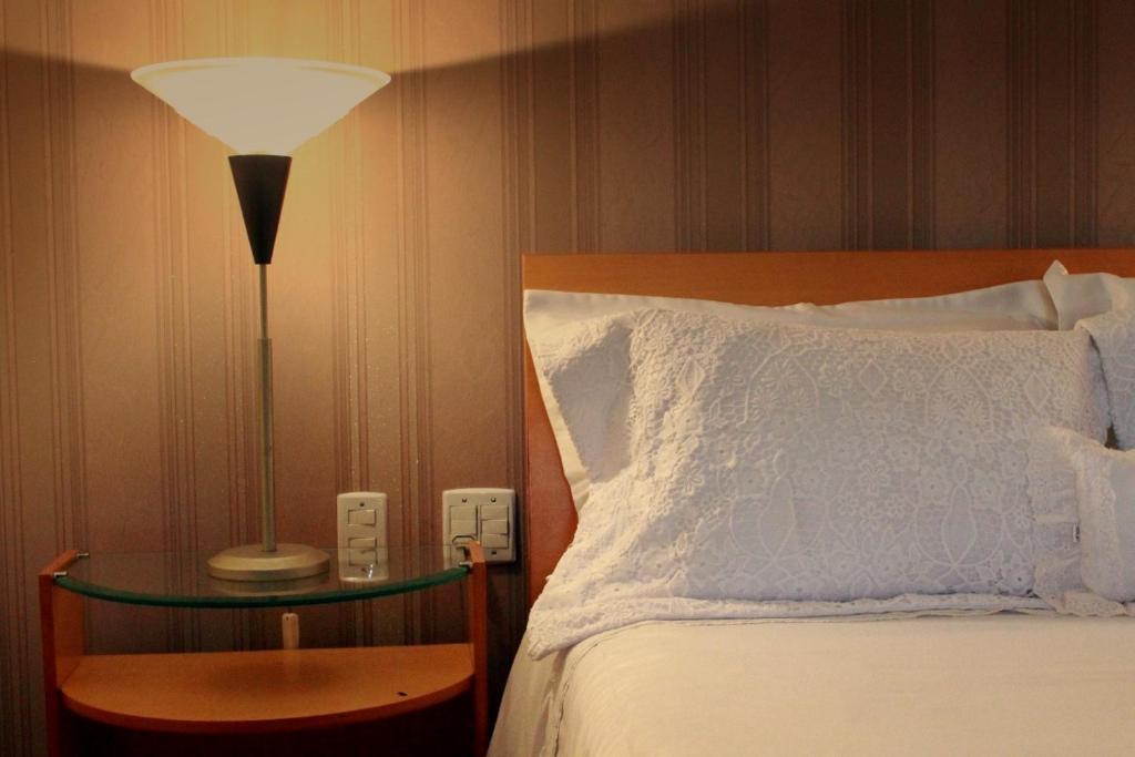 a bedroom with a bed and a lamp on a table at Hotel Caiçara Bistrô e Eventos Ltda in Itaperuna