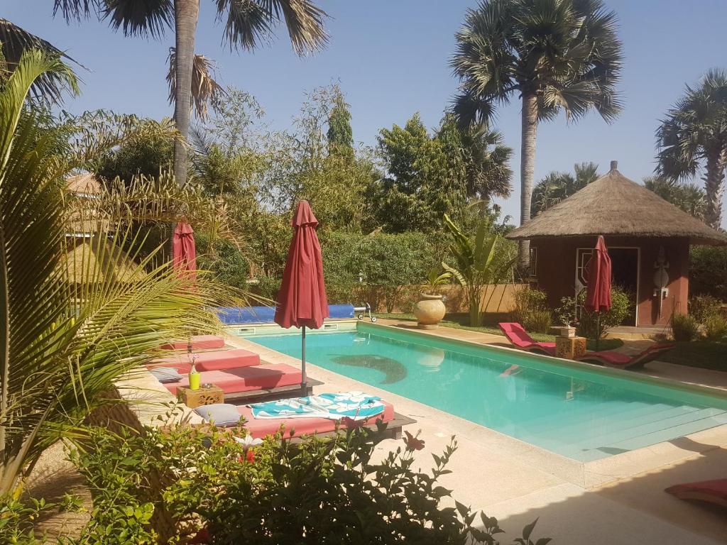 a swimming pool with chairs and an umbrella and a resort at Keur Palmier Saly in Saly Portudal