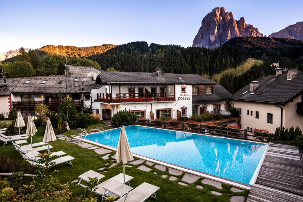 um hotel com piscina e montanhas ao fundo em Vitalpina Hotel Dosses em Santa Cristina in Val Gardena