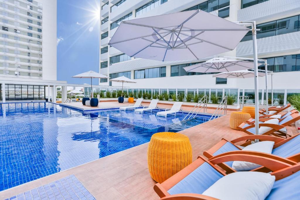 a swimming pool with chairs and umbrellas next to a building at Transamerica Executive Campos dos Goytacazes in Campos dos Goytacazes