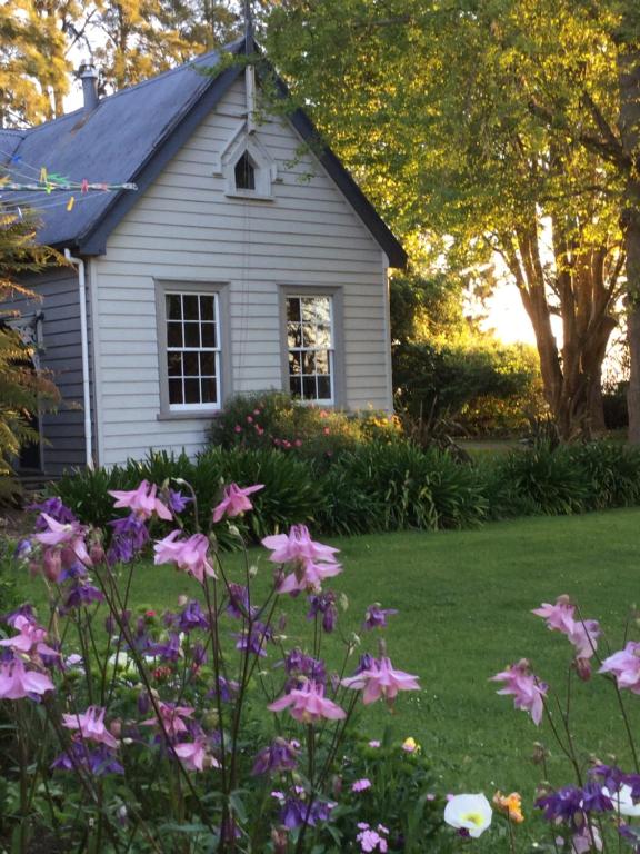 a white house with flowers in the yard at The Old School House in Te Awamutu