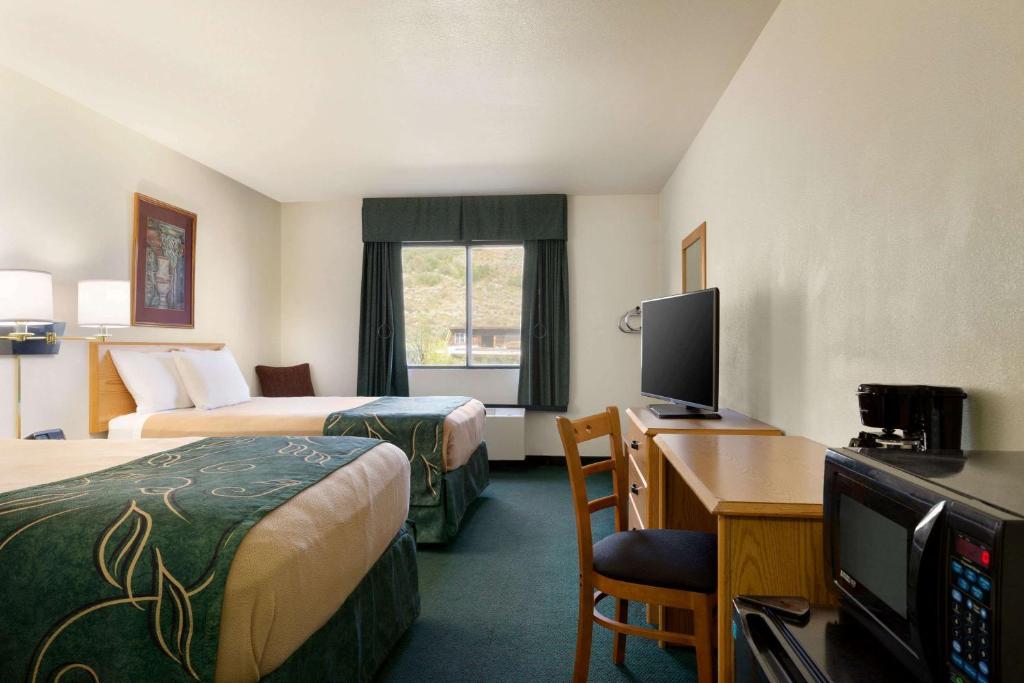 a hotel room with two beds and a desk with a television at Travelodge by Wyndham Yampa in Yampa