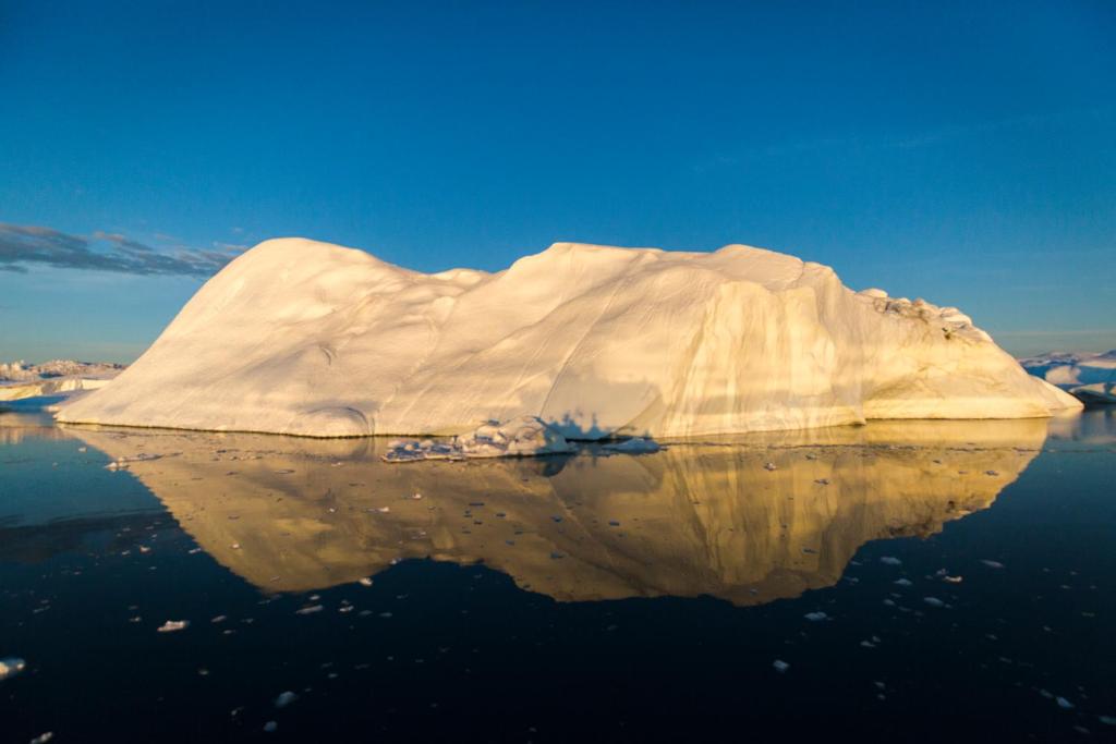 an iceberg in the water with its reflection in the water at Hotel Icefiord in Ilulissat
