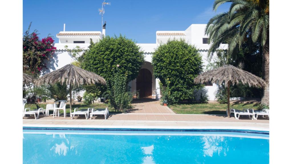 a pool with chairs and umbrellas in front of a building at Villa Nieves is a beautiful villa set in a rural location yet it is still only a 5 minute drive from San Antonio and San Rafael in San Antonio