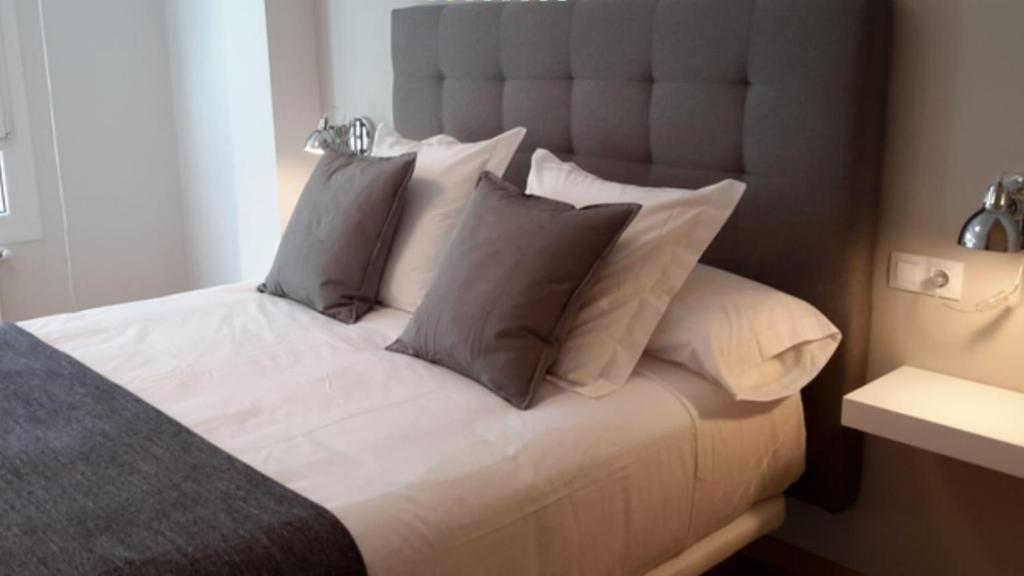 1 dormitorio con 1 cama con sábanas y almohadas blancas en APARTAMENTOS PORTA NOVA, en Lugo