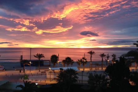 a sunset over a beach with palm trees and the ocean at 1 Linea Playa San Juan in Alicante