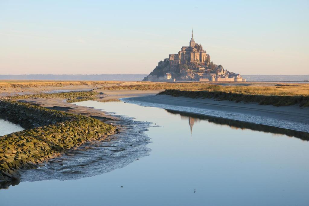 an island in the water with a castle in the background at Le Saint Aubert in Le Mont Saint Michel