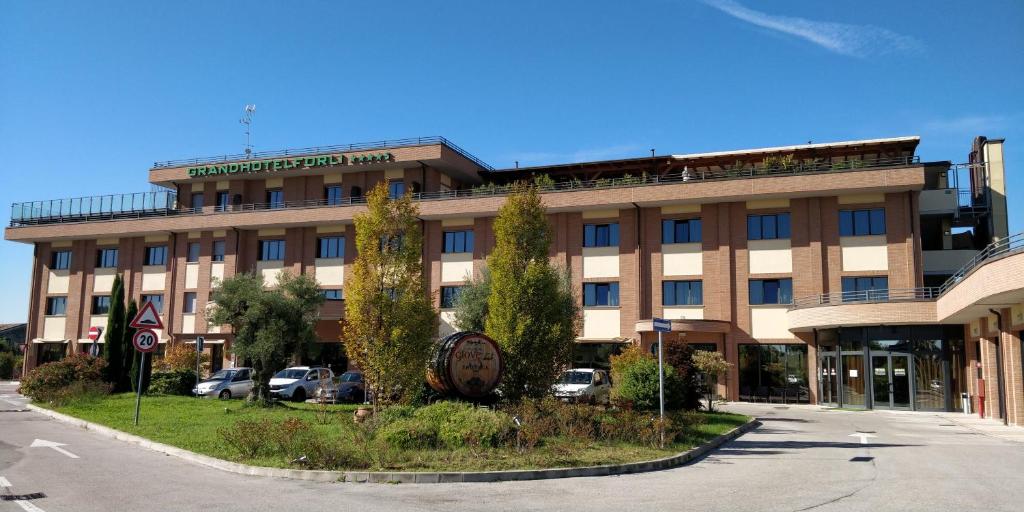 un grand bâtiment avec des voitures garées devant lui dans l'établissement Grand Hotel Forlì, à Forlì