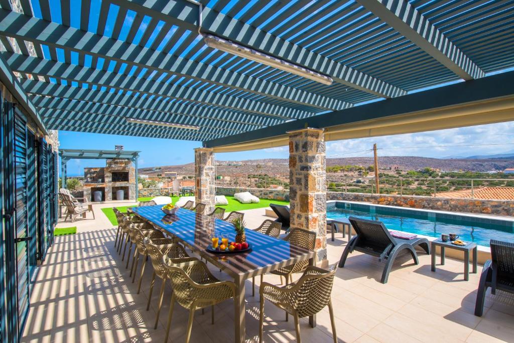 eine Terrasse mit einem Tisch, Stühlen und einem Pool in der Unterkunft Mandy Luxury Villa Cretevasion in Anópolis