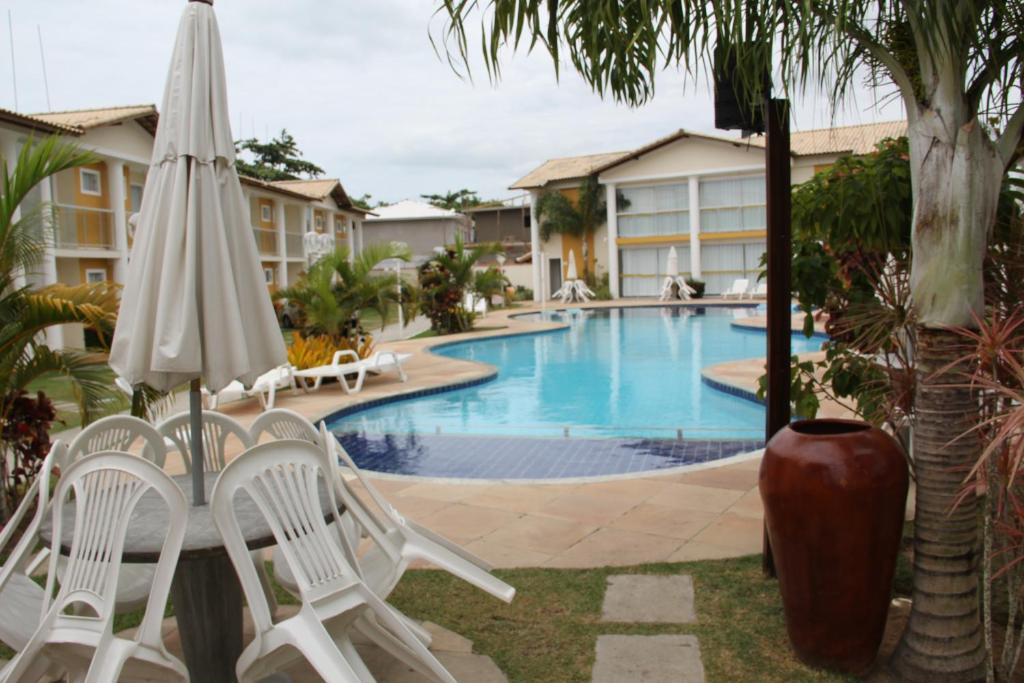 una piscina con sillas blancas y sombrilla en Apartamento Mont Carmelo, en Porto Seguro