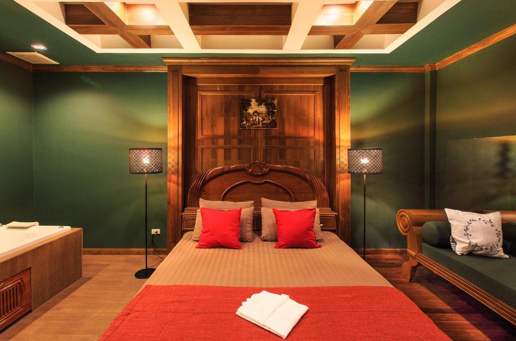 A dark green bedroom with a carved wooden bed, red accents and a separate sofa.