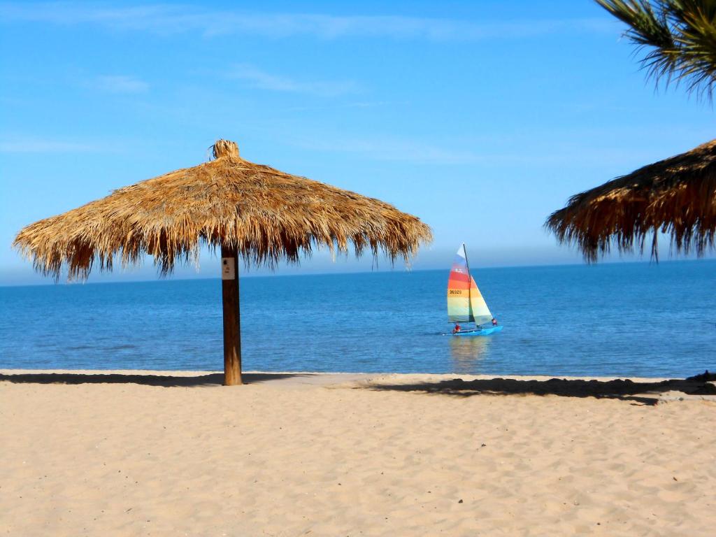 una sombrilla de paja en una playa con un velero en el océano en #36 Bungalow Seaside Hotel & Victors RV Park, en San Felipe