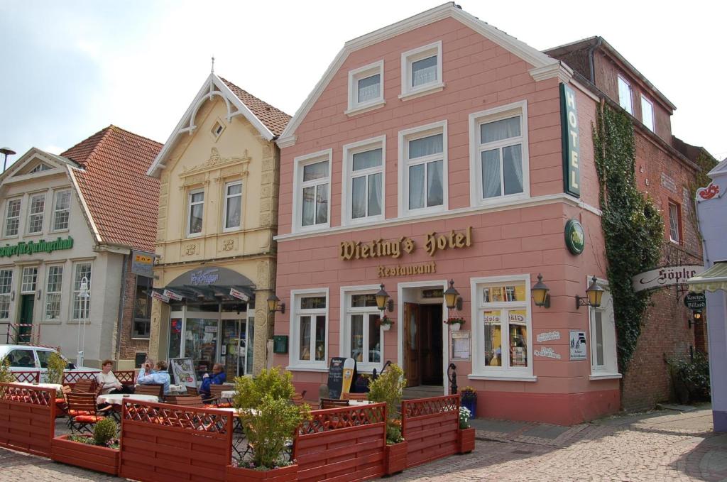 Un bâtiment rose avec des personnes assises à l'extérieur dans l'établissement Wieting´s Hotel, à Esens