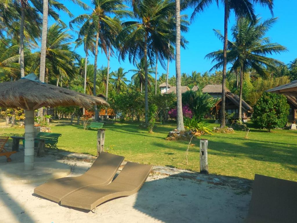 a hammock and an umbrella on a beach with palm trees at Ary's Lagoon Bungalow & Hotel in Karimunjawa