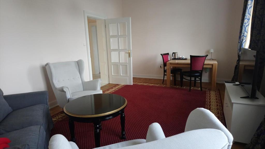 Spacious sitting room with armchairs, round black coffee table, red carpet and a desk with kettle.