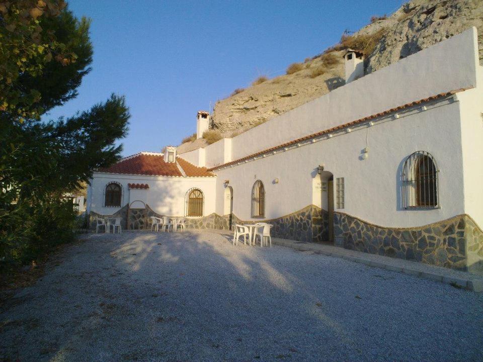 biały budynek ze stołami i krzesłami przed nim w obiekcie Casas Cueva Paloma w mieście Los Carriones