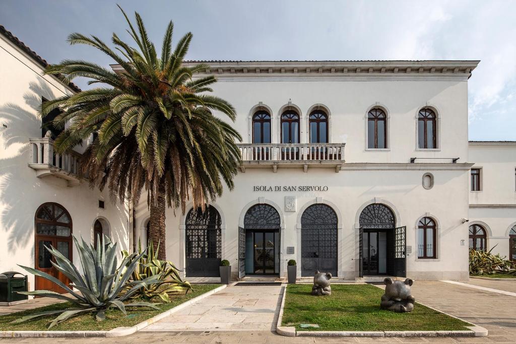 un edificio con una palmera delante de él en Isola di San Servolo - Centro Soggiorno, en Venecia