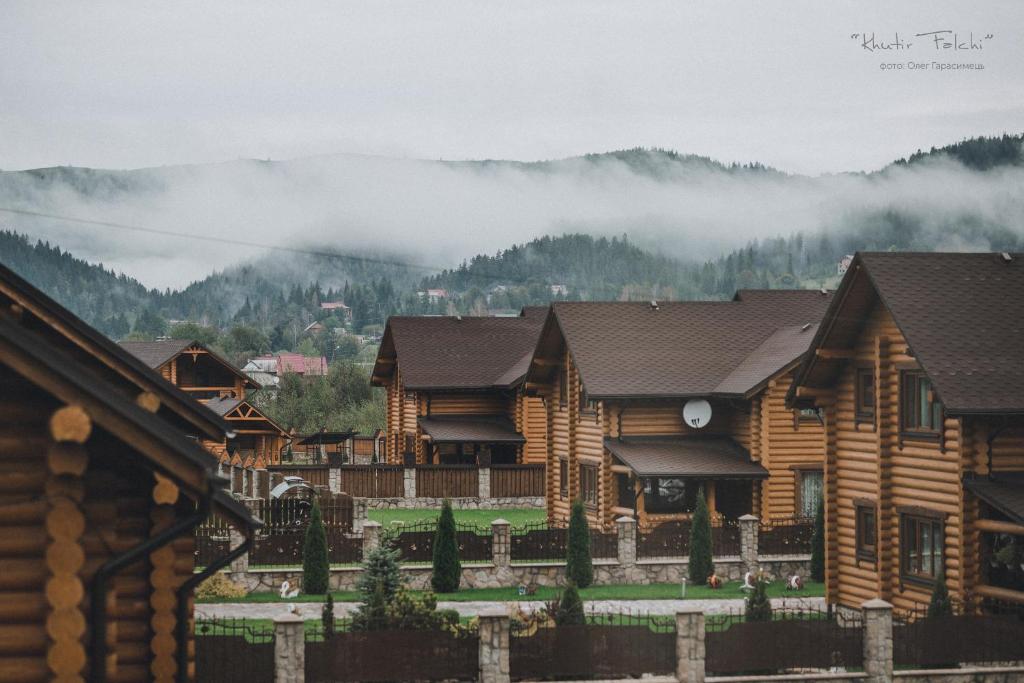 un grupo de casas de madera con montañas en el fondo en Khytir Falchi en Mykulychyn