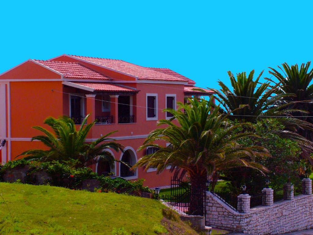 una casa rosa con palmeras delante en Villa Voula en Agios Stefanos