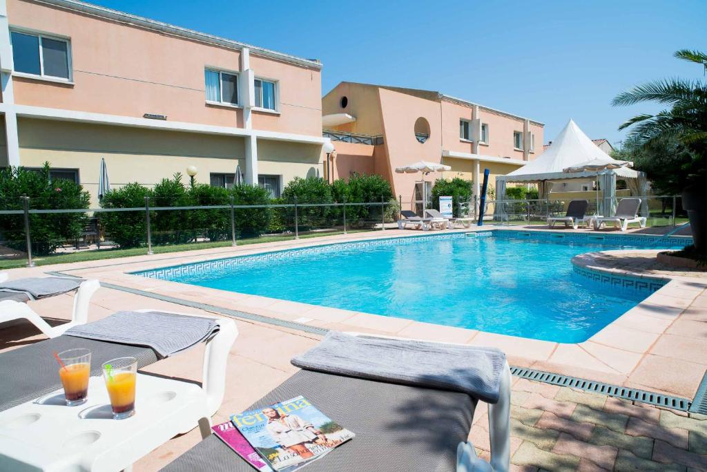 a swimming pool with two glasses of orange juice next to a hotel at Hôtel Ariane in Istres