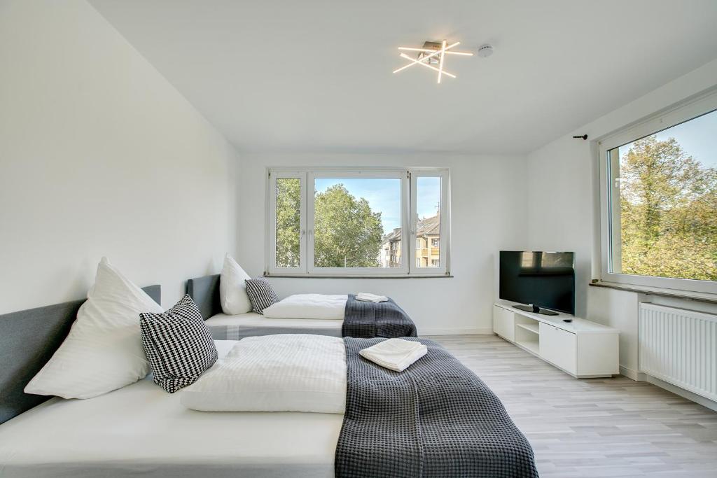 a white bedroom with two beds and a television at Stay Here ND Apartments in Krefeld