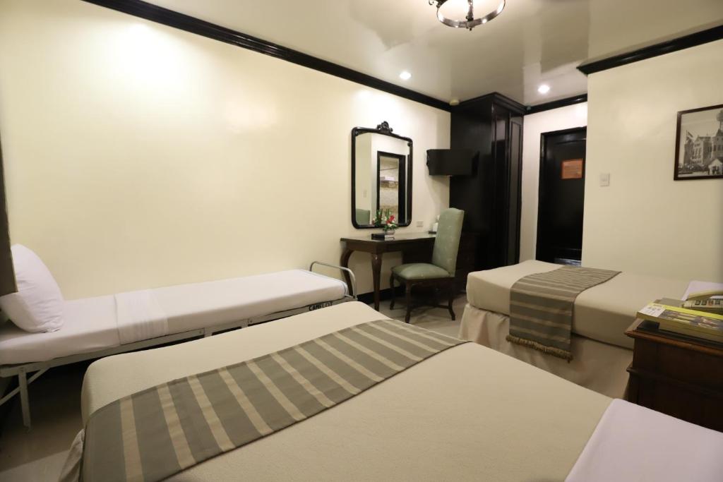 um quarto com 2 camas, um espelho e uma secretária em Camelot Hotel em Manila