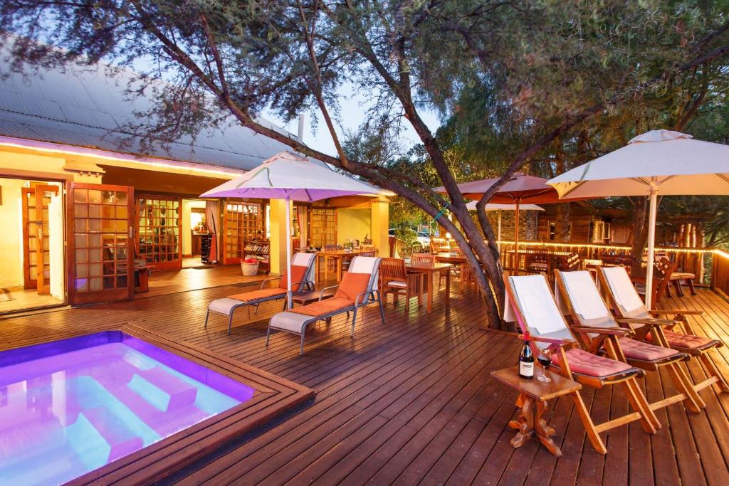 a deck with a swimming pool and chairs and umbrellas at Riverside Guest Lodge in Oudtshoorn