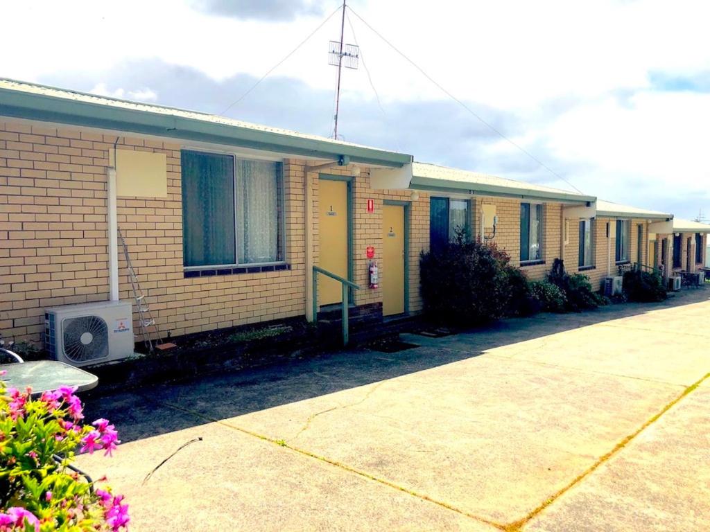 une rangée de maisons avec des portes jaunes et des fleurs violettes dans l'établissement Augusta Escape Holiday Units, à Augusta