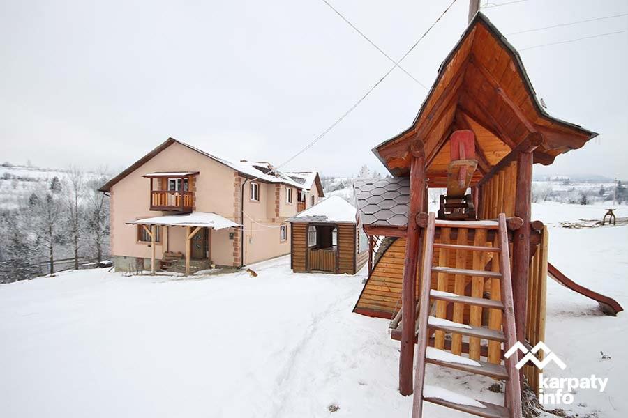 a small wooden house with a playground in the snow at на гірському схилі in Slavske