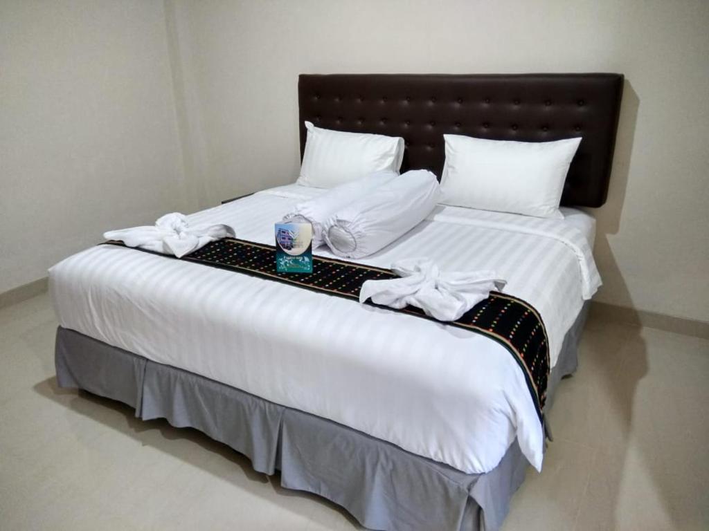 uma cama grande com lençóis brancos e uma vela em Victory Hotel em Ruteng