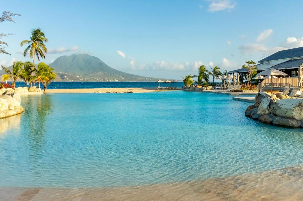 a swimming pool next to a beach with palm trees at Park Hyatt St. Kitts in Christophe Harbour