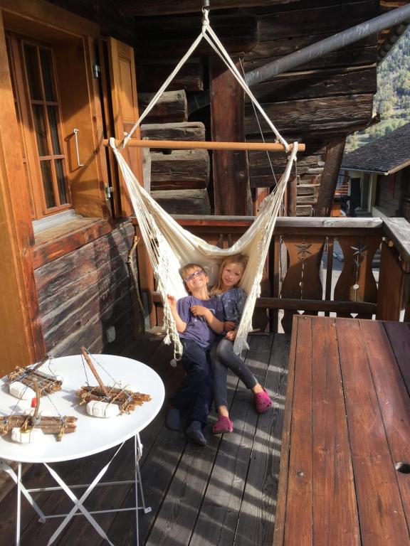 two children sitting in a hammock on a porch at Chalet Michel in Bruson