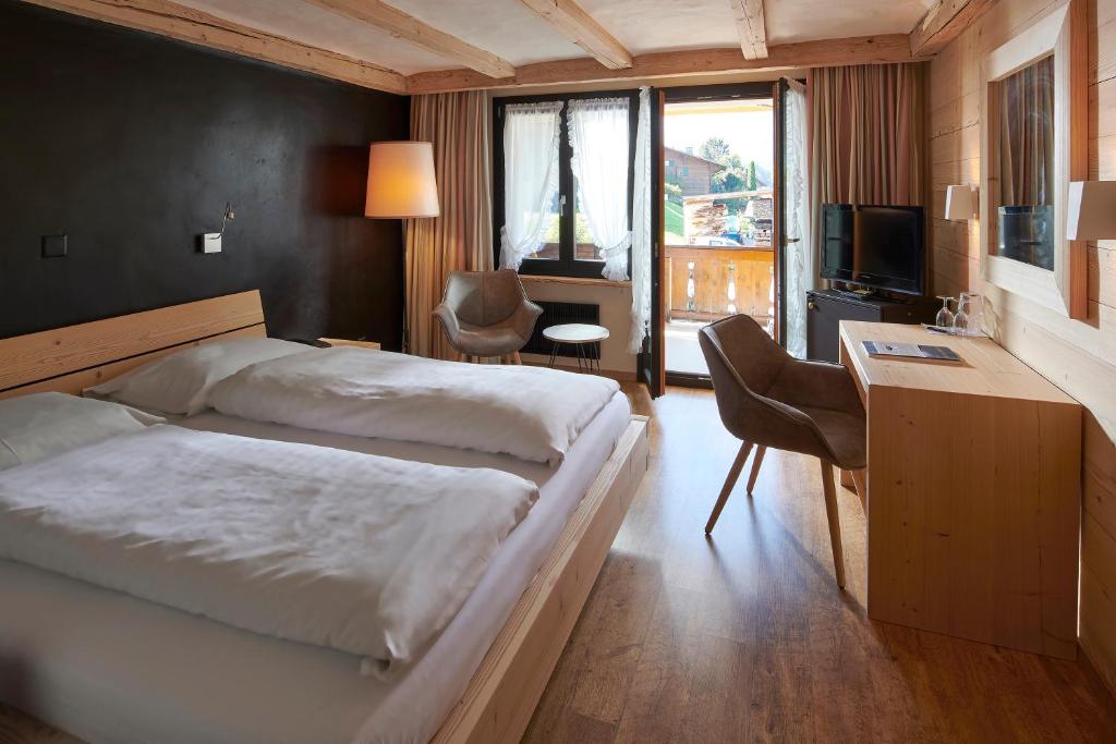 a bedroom with two beds and a desk and a television at Hotel Alphorn in Gstaad