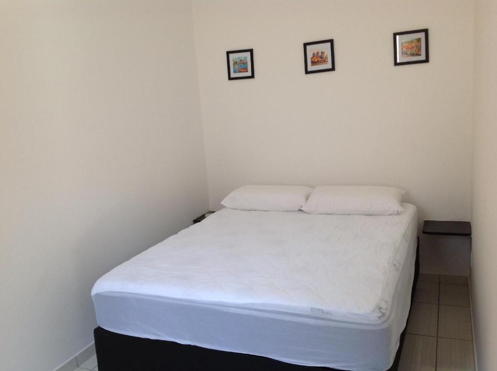a small bedroom with a white bed with two pillows at Chalés Ubatuba 102 - P. Itaguá in Ubatuba