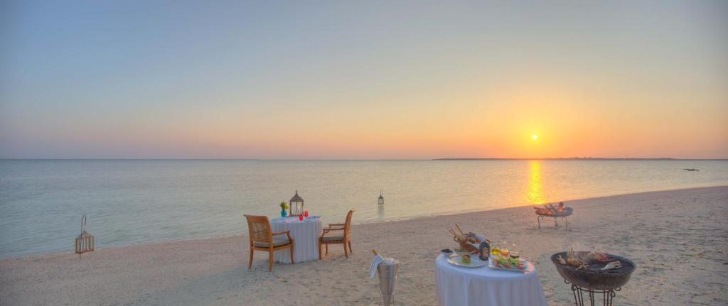 a table and chairs on the beach at sunset at The Residence Zanzibar in Kizimkazi