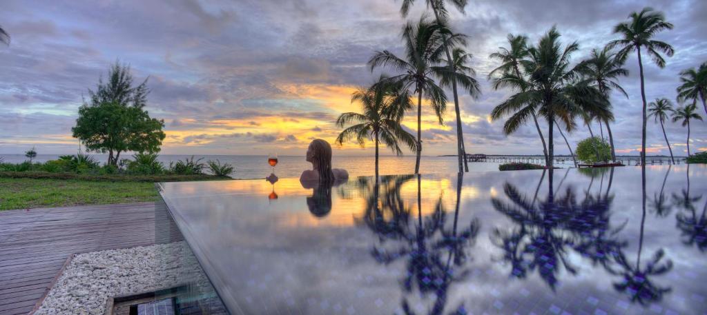 een uitzicht op een zwembad met palmbomen en een zonsondergang bij The Residence Zanzibar in Kizimkazi