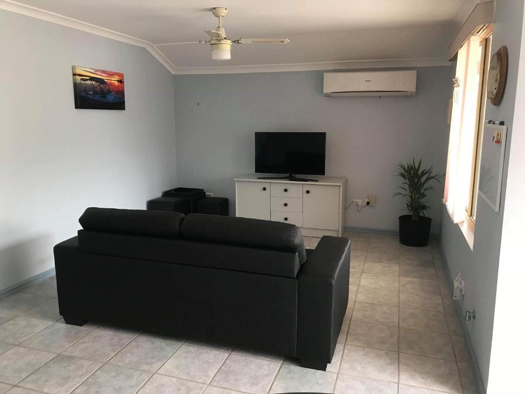 uma sala de estar com um sofá preto e uma televisão em Guesthouse on Dolphin em Safety Bay