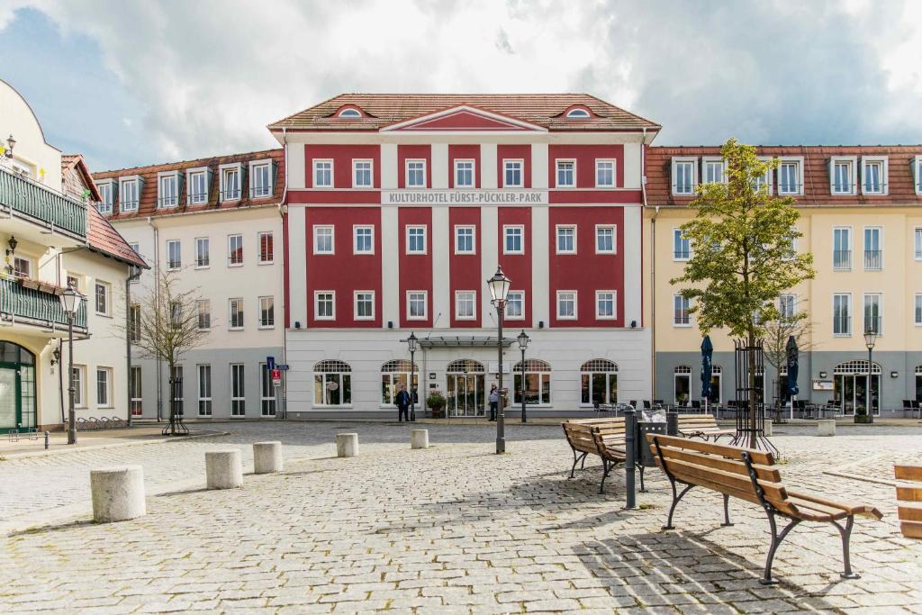 um grande edifício vermelho com bancos à sua frente em Kulturhotel Fürst Pückler Park em Bad Muskau