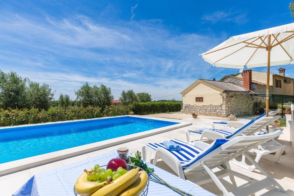 eine Villa mit einem Pool mit Stühlen und einem Sonnenschirm in der Unterkunft Stone House Rita with Pool in Poreč