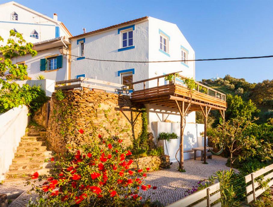 a white house with a balcony and red flowers at Romantic riverside retreat in Odemira