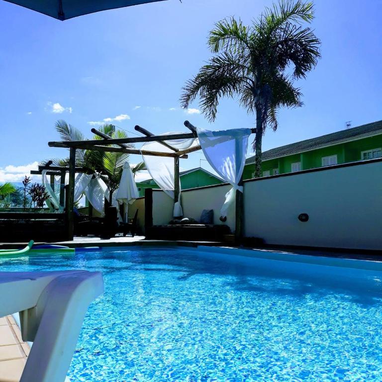 a swimming pool in front of a building with a palm tree at Recanto Rustico Itapoá in Itapoa