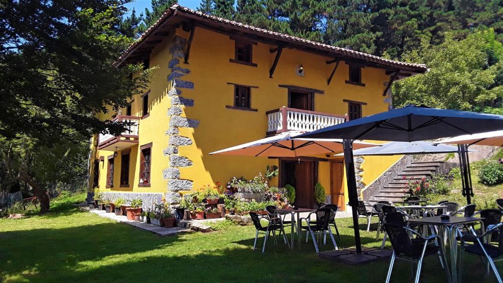 a yellow house with tables and umbrellas in front of it at Albergue Mandoia Aterpetxea in Aránzazu Celaya