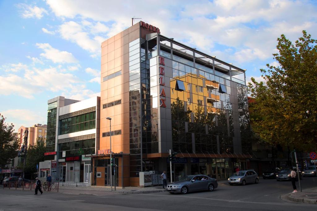 un edificio de cristal alto con coches estacionados frente a él en Hotel Relax en Tirana