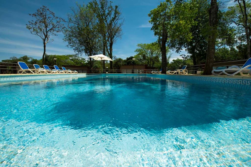 a large swimming pool with chairs and an umbrella at Gran Hotel Tourbillon & Lodge in Puerto Iguazú