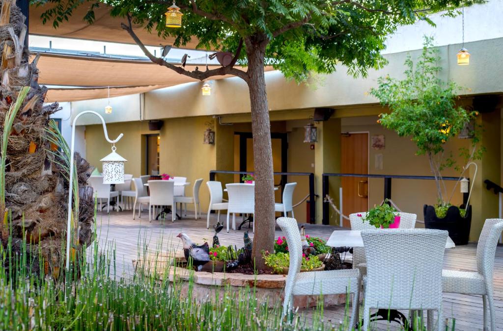 a patio with tables and chairs and a tree at C Hotel Neve Ilan in Neve Ilan