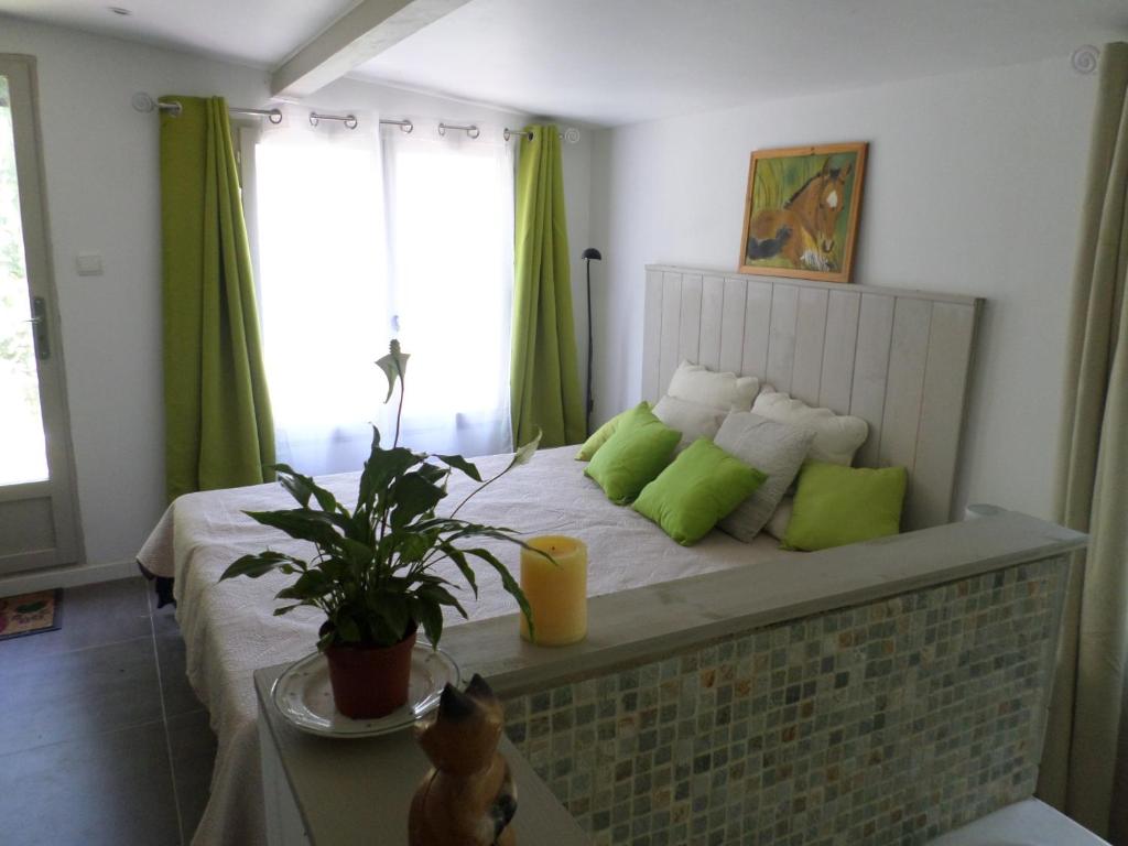 ein Schlafzimmer mit einem Bett mit grünen Kissen und einer Pflanze in der Unterkunft Chambre d'Hôte - Mas Le Barret in Arles