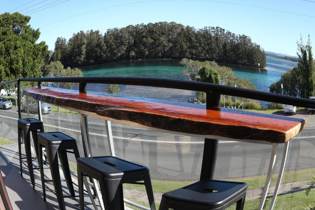 a table and stools on a balcony with a view of the water at Wallis View 13 in Forster