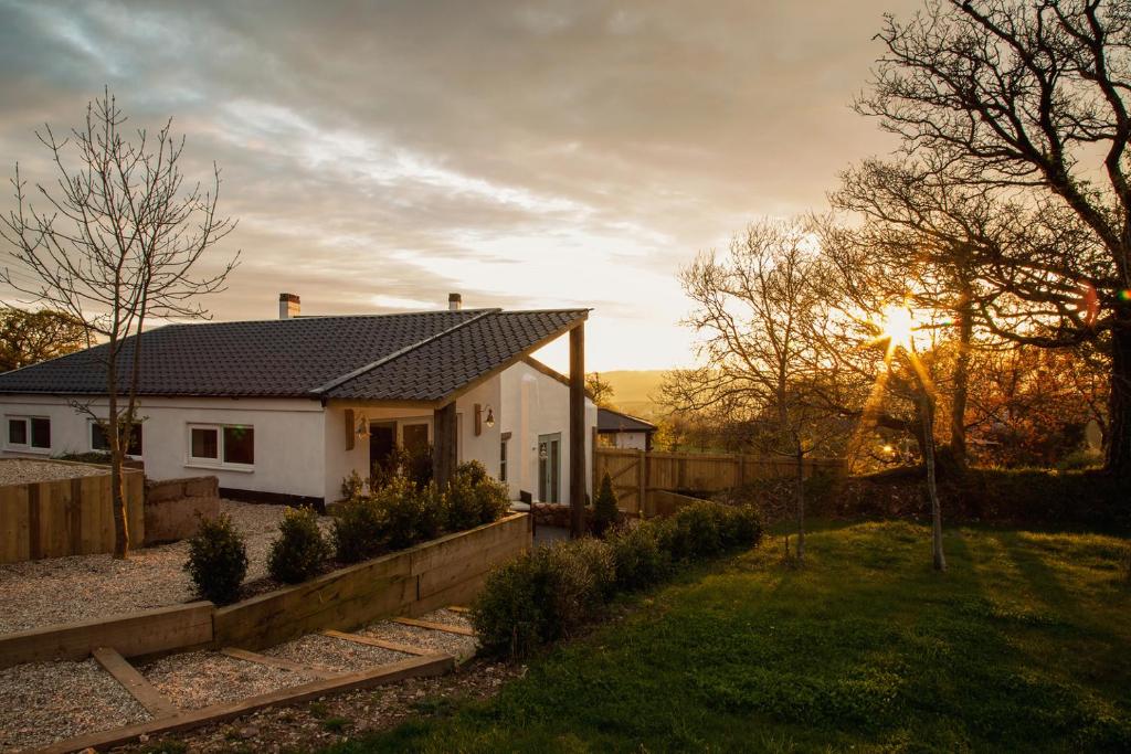 une maison blanche avec le coucher de soleil derrière elle dans l'établissement The Burrow at Burrow Wood Farm, à Ottery St Mary